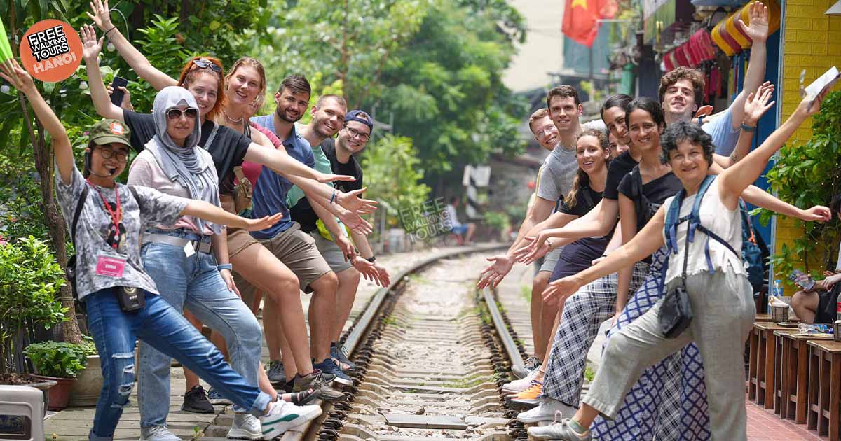 Group of cheerful tourists posing on Hanoi Train Street with local guide during a free walking tour